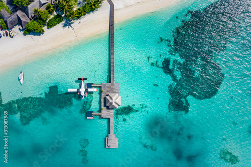 Aerial view of water bungalow and blue sea background in Maldives. Seaplane and wooden Dhoni boats on tropical lagoon. Aerial landscape, exotic travel and vacation concept. Drone view of beach scene