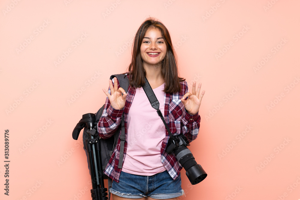 Young photographer girl over isolated pink background showing an ok sign with fingers Young photographer girl over isolated pink background showing an ok sign with fingers