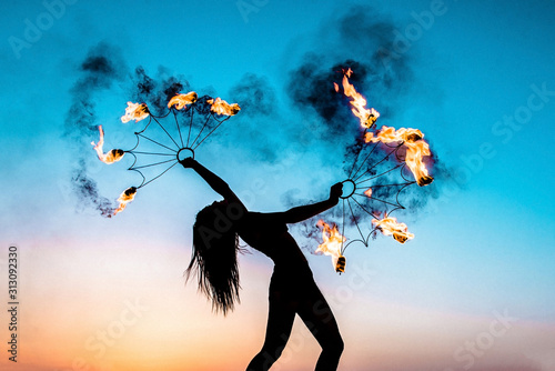 Fire show at sunset. Silhouette of a girl with burning torches