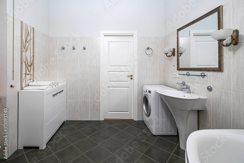 Modern interior of bathroom in light tones with black tile on the floor. Washing machine. White dresser.