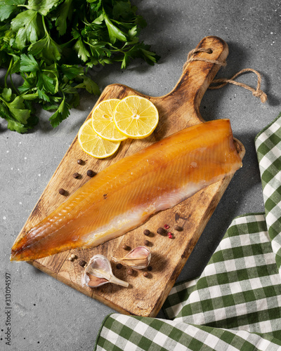 Cold smoked muksun fish on a wooden Board on a gray kitchen table. Whole fillet of fish whitefish or muksun closeup photo