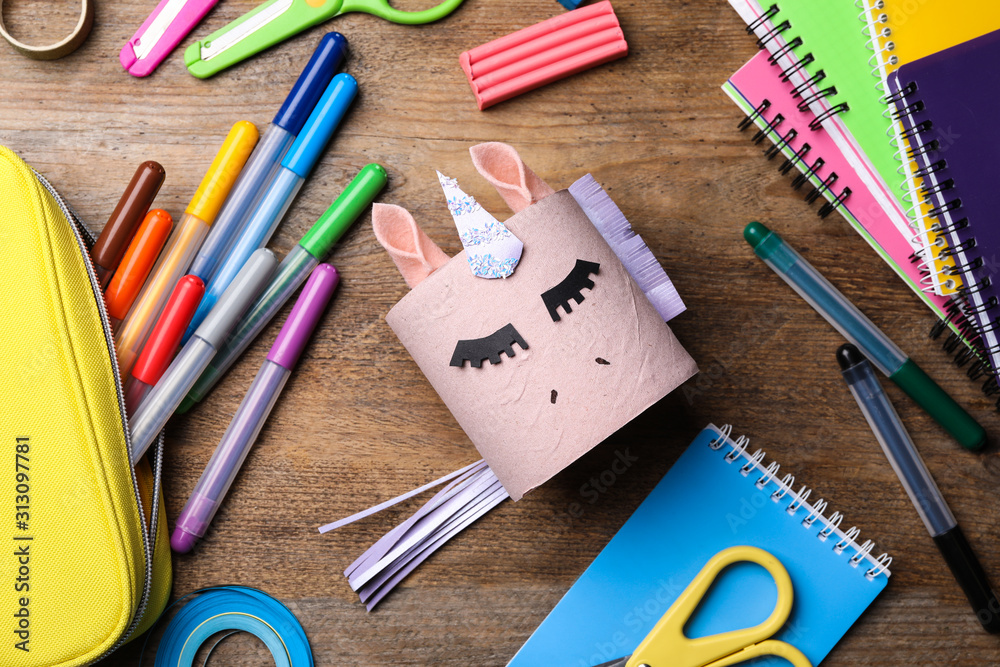 Toy unicorn made of toilet paper roll among stationery on wooden table, flat lay Toy unicorn made of toilet paper roll among stationery on wooden table, flat lay