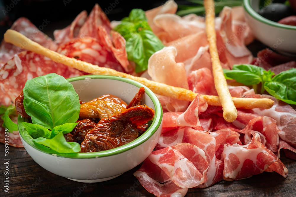 Italian meat appetizers and on a wooden plate. Wine snack Antipasto-salami, prosciutto, slices ham, beef jerky and bread sticks.