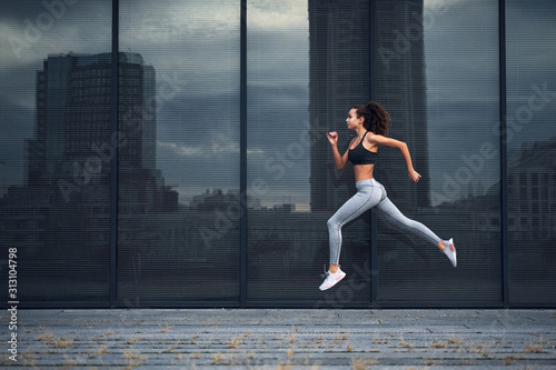 Young athletic woman running in the city, shot of girl jumps on the glass building background