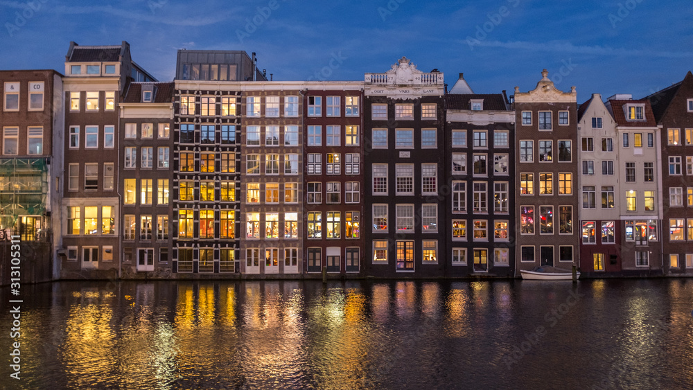 Night view of the Amsterdam Damrak canal with facades and reflections of Dutch canal houses.
