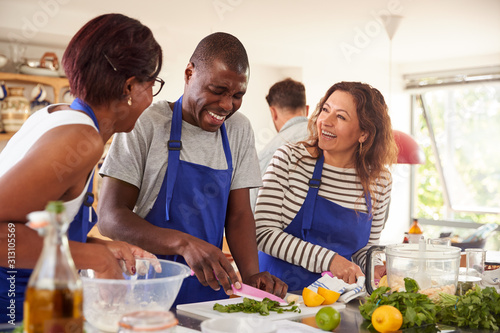 Male And Female Adult Students Preparing Ingredients For Dish In Kitchen Cookery Class