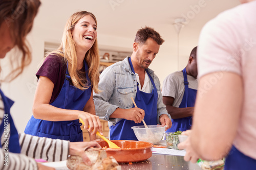 Male And Female Adult Students Preparing Ingredients For Dish In Kitchen Cookery Class photo