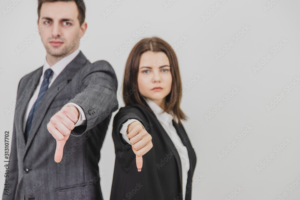 Business man and woman standing back to back, giving thumbs down, frowning. Focus on the gesture on the forefront. Business man and woman standing back to back, giving thumbs down, frowning. Focus on the gesture on the forefront.