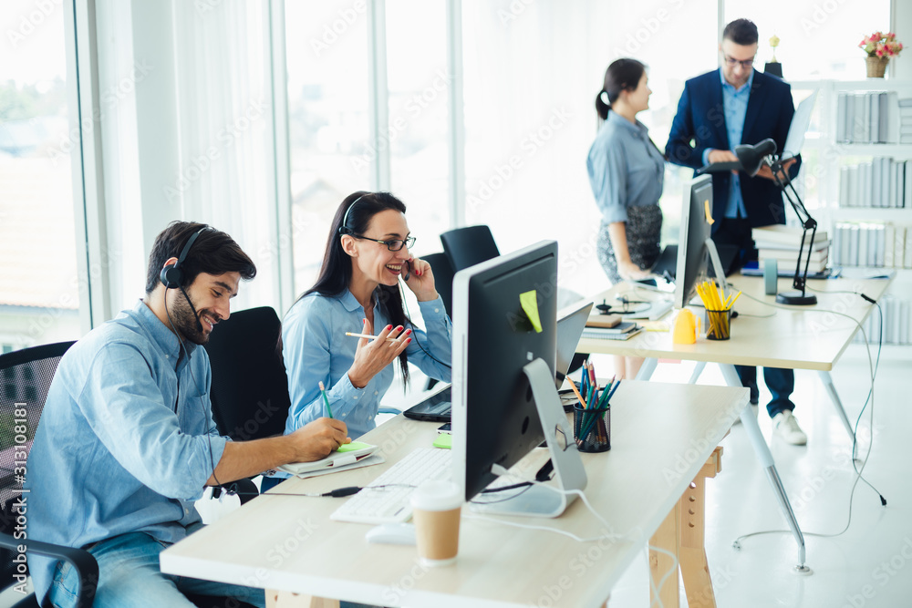 Attractive business people in headsets are smiling while working with computer in modern office Attractive business people in headsets are smiling while working with computer in modern office