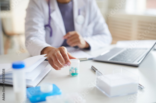 Close-up of female doctor sitting at desk and holding bottle with pills she prescribing them to her patient at hospital