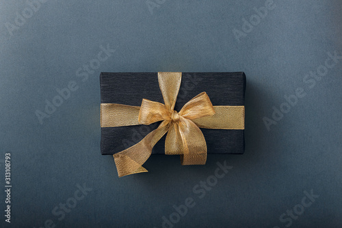 a gift wrapped in black paper and tied with a gold ribbon. expensive gift concept.