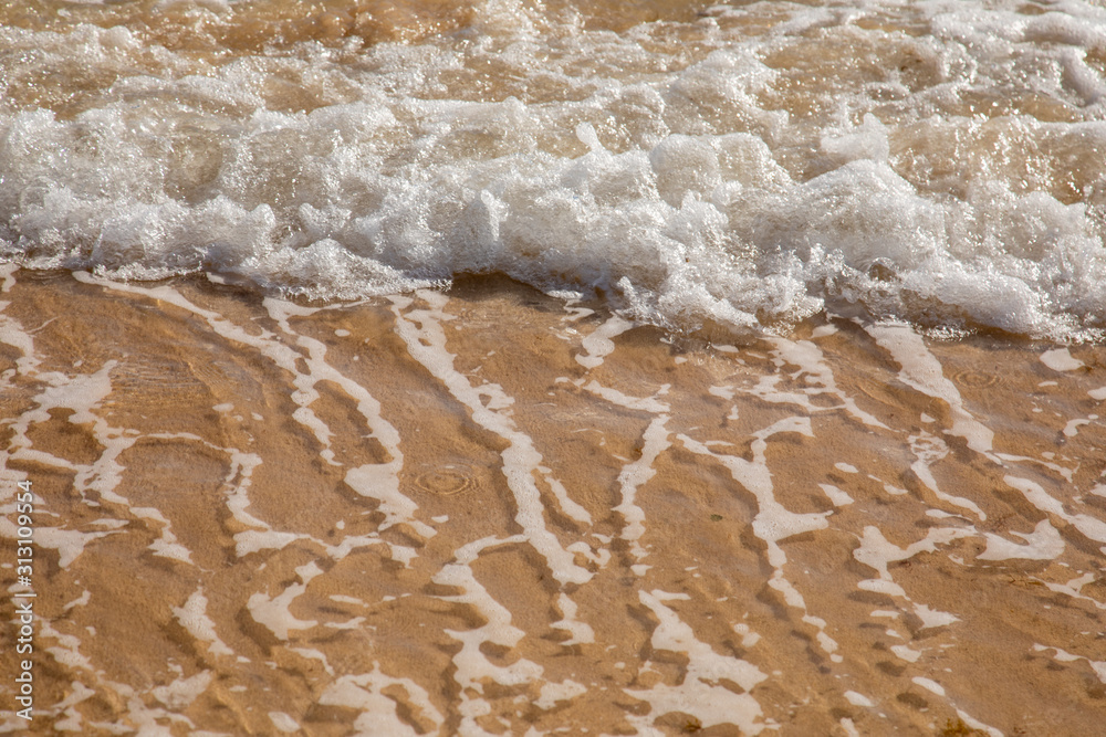 Waves breaking on an empty sand beach and spalsh producing foam - travel holiday vacation summer sun - splashing water - wavy golden yellow sand background - empty space Waves breaking on an empty sand beach and spalsh producing foam - travel holiday vacation summer sun - splashing water - wavy golden yellow sand background - empty space