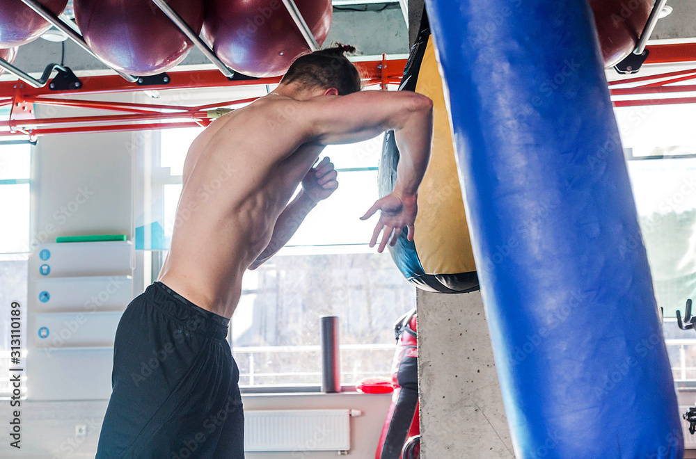shirtless muscular sportsman hitting punching bag during boxing practice in fight club