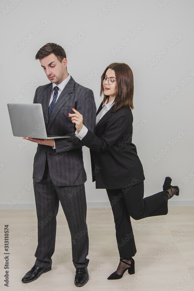 Handsome man standing, working with laptop. Woman is pointing from man's behind at something in the laptop, interfering him. Man is annoyed because of this. Handsome man standing, working with laptop. Woman is pointing from man's behind at something in the laptop, interfering him. Man is annoyed because of this.