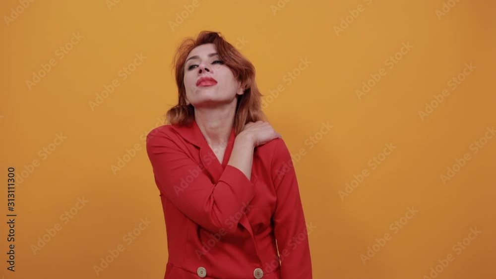 Unhappy caucasian young woman wearing fashion red jacket over isolated orange background, staying sideways, keeping hand on back, pain in muscules. People lifestyle concept. Unhappy caucasian young woman wearing fashion red jacket over isolated orange background, staying sideways, keeping hand on back, pain in muscules. People lifestyle concept.