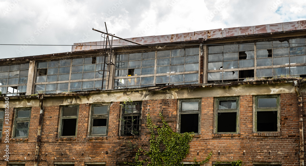 abandoned factory warehouse with broken windows and covered in green ivy plant abandoned factory warehouse with broken windows and covered in green ivy plant