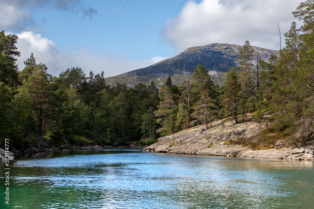 Sunny day by the cold sparkling river in pine forest mountains of Norway. Natural background with blue sky and clouds.