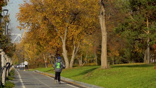 A little boy with a backpack rides a scooter in an autumn city park. Active leisure and outdoor sport for children. 4k footage.