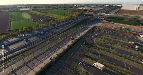 Aerial view over commercial area in the suburbs of Barcelona, Spain, showing a parking with small palm trees, and highway roads, a bridge and fields in this rural background