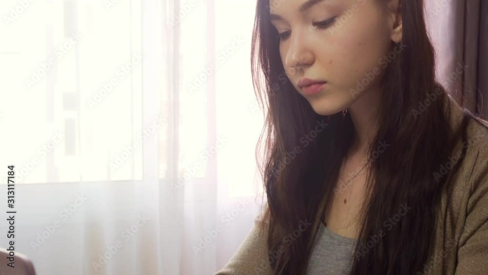 A young brunette woman with curly hair sits at a table and writes on a laptop keyboard. The concept of work at home. A young brunette woman with curly hair sits at a table and writes on a laptop keyboard. The concept of work at home.