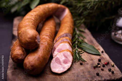 Φωτογραφία Rings of traditional, tasty pork smoked sausage on a wooden cutting board on a stony countertop