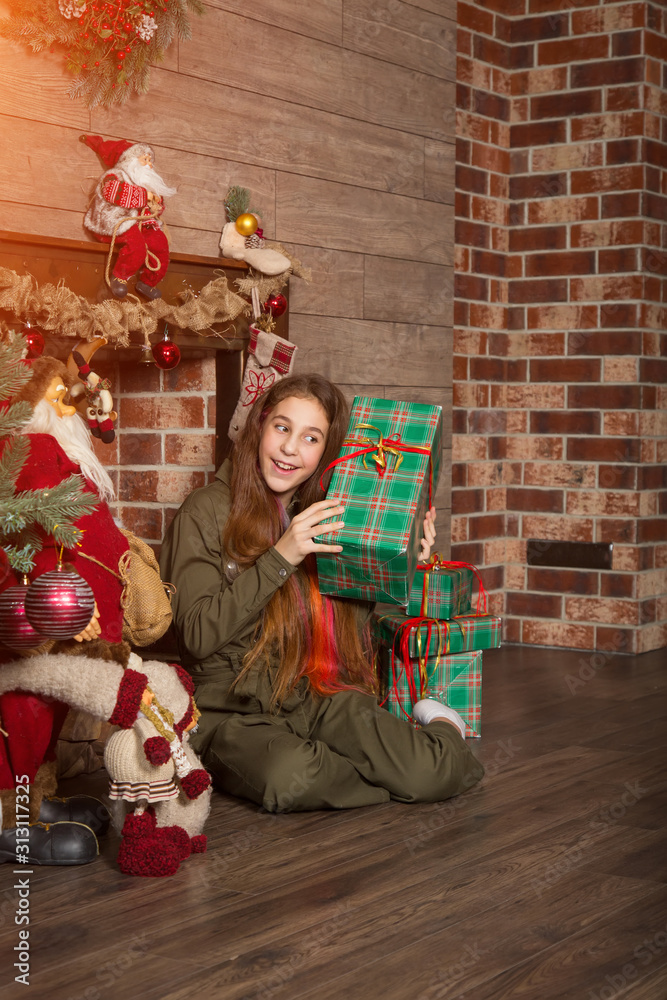 Beautiful girl with Christmas gifts in hands sitting near the fireplace with New Year decorations. Vertical image.