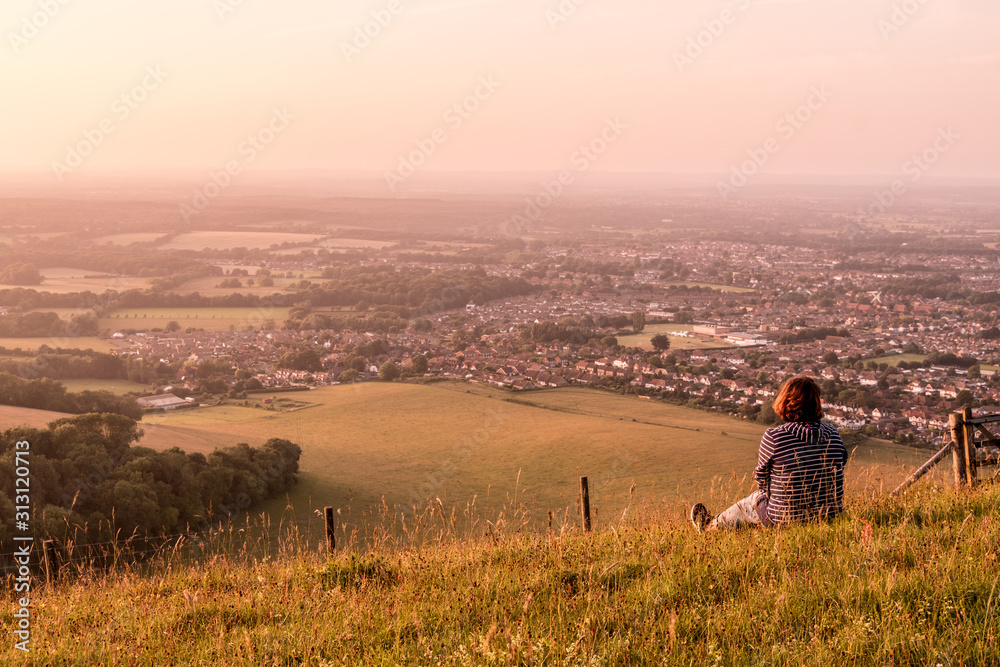 Single woman sitting on a hill looking out over the countryside in East Sussex on a summer's evening