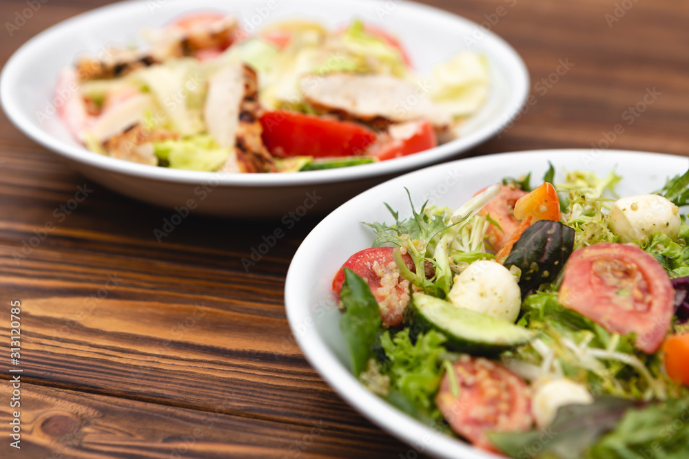 white deep plates with fresh salad ingredients mixed with sauce placed on an attractive background. A place for a menu, banner or advertisement white deep plates with fresh salad ingredients mixed with sauce placed on an attractive background. A place for a menu, banner or advertisement