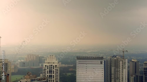 Slow aerial view of the highly urbanized city of Manila, Philipines, showing huge skyscappers among smaller buildings and construction cranes, in a cloudy light