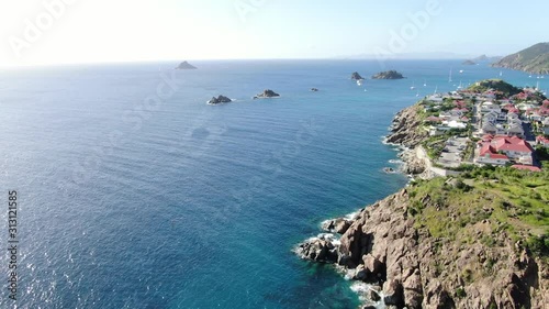 Slow aerial view of the coast of St-Barthelemy island, showing residential constructions, calm ocean waves on the rocky seashores on a sunny day photo