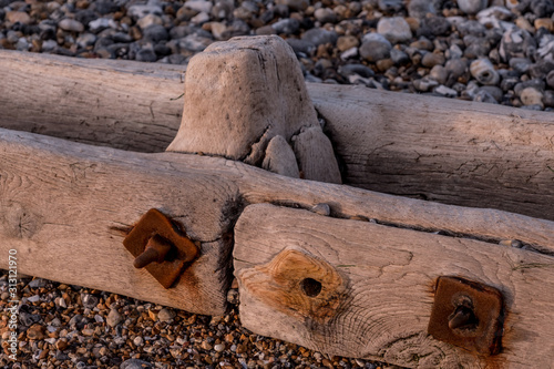 Sections of a wooden groyn on a pebbled beach joined by rusty bolts photo