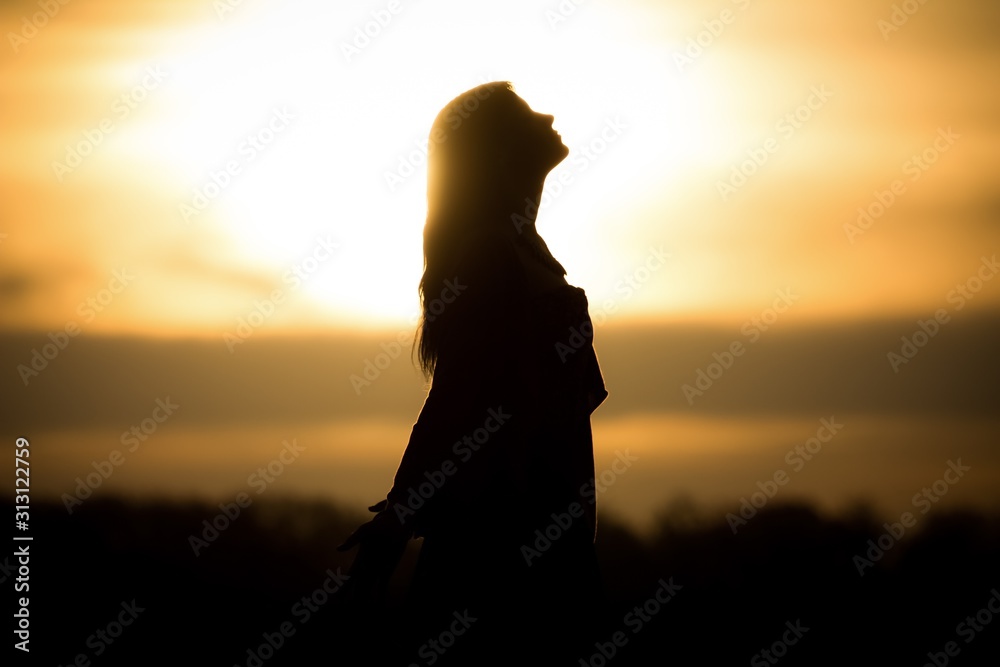 Youth woman soul at orange sun meditation awaiting future times. Silhouette in front of sunset or sunrise in summer nature. Symbol for healing burnout therapy, wellness relaxation or resurrection