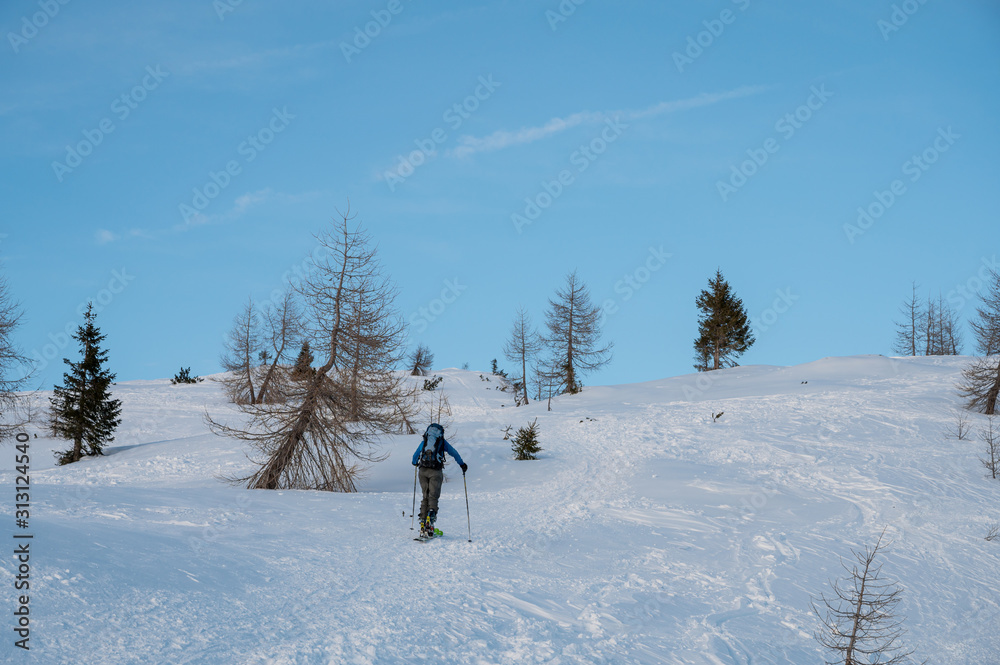 Lonely skiier ascending snowy mountain top at dusk.