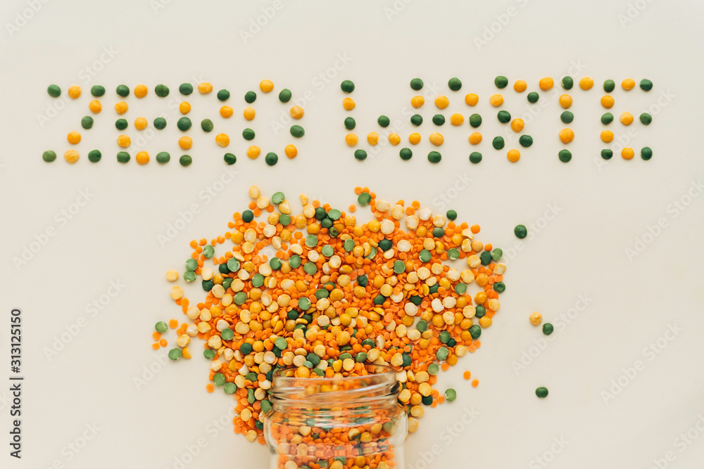 Zero waste creative text. Colorful legumes: red lentils and split peas scattered from glass jars at ivory color background.