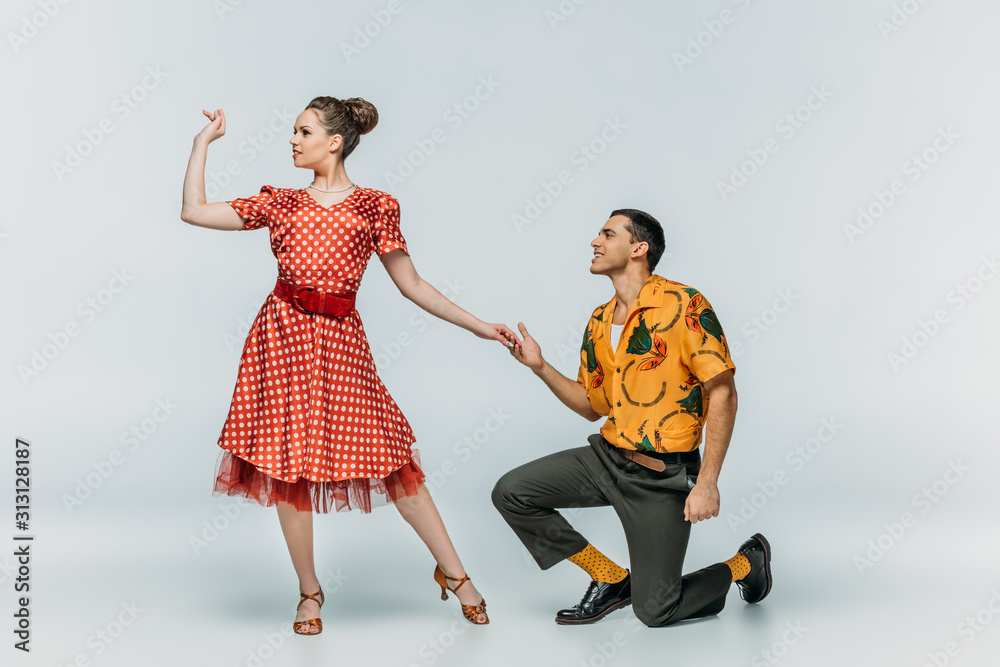 handsome man standing on knee and inviting pretty woman to dance boogie-woogie on grey background handsome man standing on knee and inviting pretty woman to dance boogie-woogie on grey background