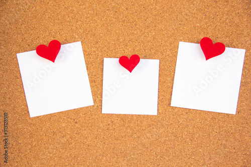 three red heart note paper on cork board