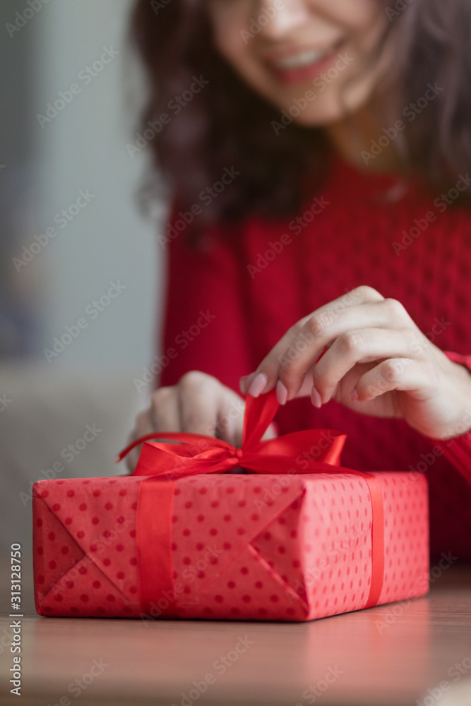 A young woman opens a present at a cafe. Red giftbox with a ribbon is being untied on a restaurant's table. Valentine's day and winter holidays concept. A young woman opens a present at a cafe. Red giftbox with a ribbon is being untied on a restaurant's table. Valentine's day and winter holidays concept.