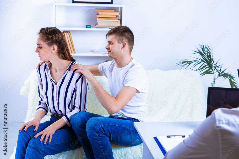 Obraz premium At the psychologist. Beautiful young couple is sitting on couch and hugging while doctor is making notes