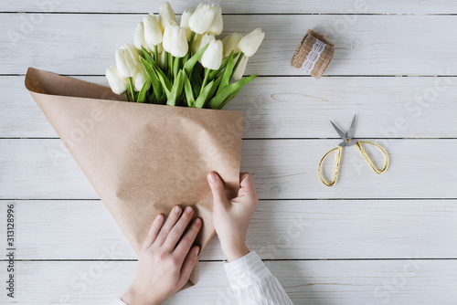 Vrouw bloemist verpakken mooi boeket van witte tulpen in pak Kraftpapier op de houten tafel. plat leggen