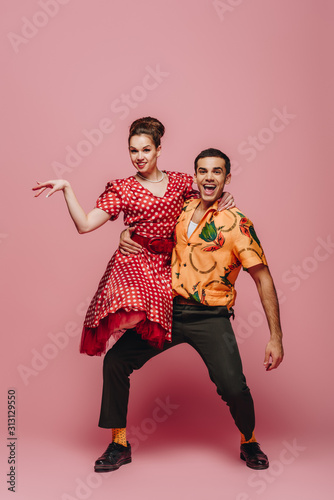 stylish dancer holding woman while dancing boogie-woogie on pink background