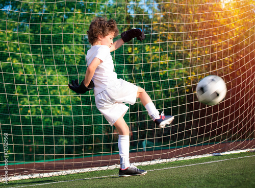 Children's soccer football - a match of young children on the football field. Young goalie. Kids - soccer champion. Boy goalkeeper in football sportswear on stadium with ball. Sport concept.