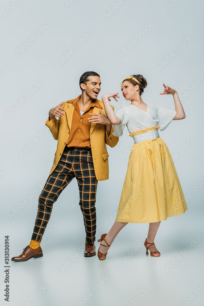 cheerful dancers looking at each other while dancing boogie-woogie on grey background