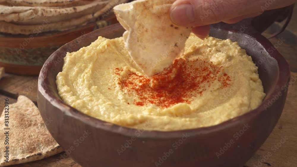 Hand dipping a pita chip into a delicious bowl of hummus.
