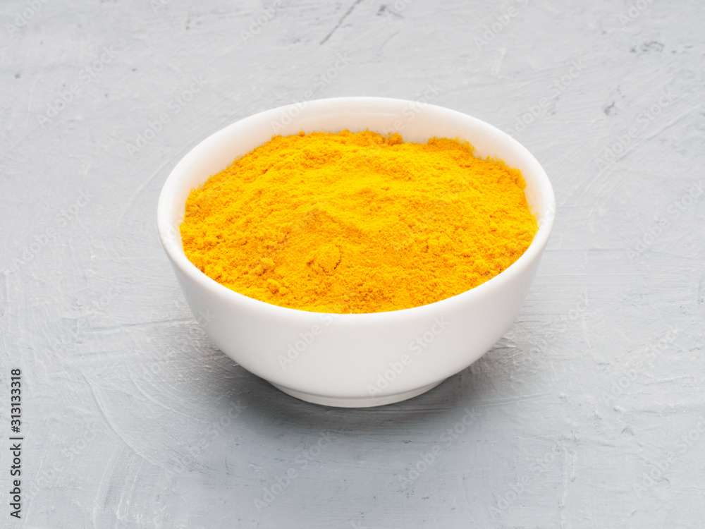 Spice turmeric in white cup on gray concrete and beige fabric background. Diet and weight loss concept