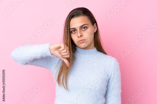 Teenager girl with blue sweater over isolated pink background showing thumb down sign