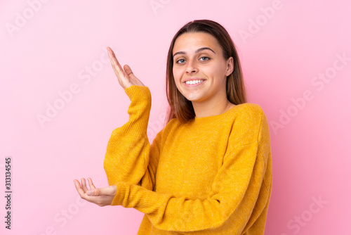 Teenager girl with yellow sweater over isolated pink background extending hands to the side for inviting to come