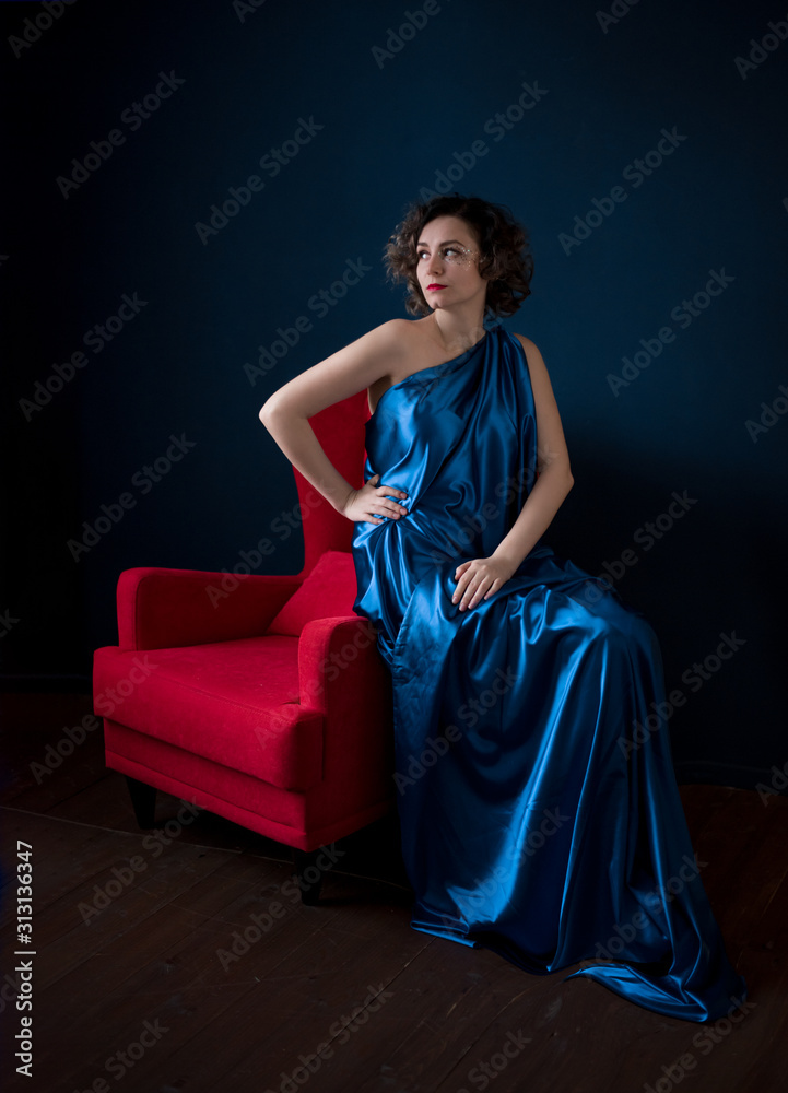 Beautiful girl sitting on red armchair on the dark blue background. Beautiful girl sitting on red armchair on the dark blue background.