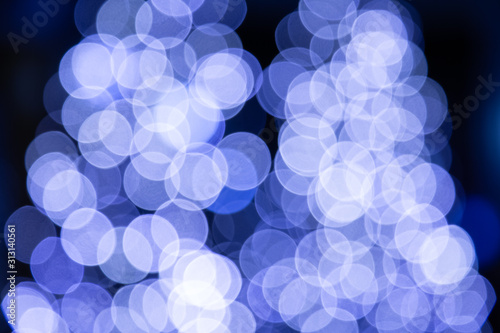 A picture of a multicolored bokeh light on a pedestrian street decorated on a tree from a lamp or car light. Using the camera lens makes the image blur beautiful in the natural black background.