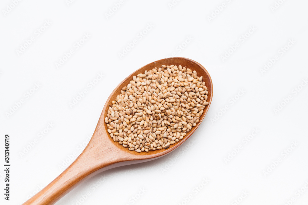Toasted Sesame seeds in wooden spoon on white Toasted Sesame seeds in wooden spoon on white