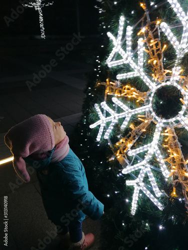 cute little baby in baby against decorated christmass tree. top view, close up, outdoor photography at night.